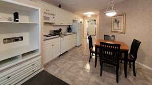 A compact kitchen with white cabinets, a stove, and a dining area with a table and chairs. - Mountain View Condo with Sofabed and Aircon (Fairmont Hot Springs)