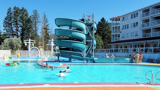 A swimming pool with a multi-tiered water slide and a building with balconies in the background. - Mountain View Condo with Sofabed and Aircon (Fairmont Hot Springs)