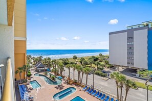 A resort with a pool area, palm trees, and a view of the beach. - New, Oceanview Suite - Caravelle 504 (Myrtle Beach)