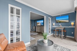 A living room with a large window, a dining area with a TV, and a kitchen in the background. - New, Oceanview Suite - Caravelle 504 (Myrtle Beach)