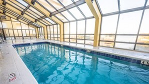 Una piscina interna con pareti in vetro trasparente, un bordo piastrellato e una scala che scende nell'acqua.