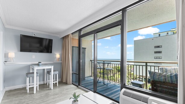 Una moderna camera d'albergo con un ampio balcone, una TV a schermo piatto, un tavolino con due sedie e un divano.