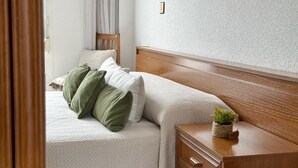Une chambre avec deux lits, une tête de lit en bois, une table de chevet avec une plante et un interrupteur sur le mur.