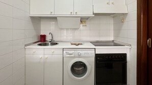 Une cuisine compacte avec des meubles blancs, un lave-vaisselle, une machine à laver et une cuisinière.