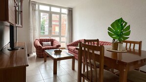 Un salon comprenant une table à manger, deux canapés rouges, un meuble TV en bois et une grande fenêtre avec des rideaux.