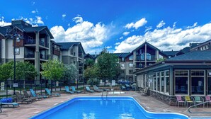 A swimming pool with lounge chairs and a building with multiple balconies in the background.