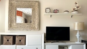 Ett vardagsrum med en vit möbel för underhållningssystemet, en platt-TV, dekorativa föremål och en lampa.
