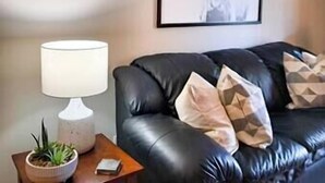 A living room with a black leather sofa, a white lamp, a framed artwork of a bull's head, and a small potted plant.