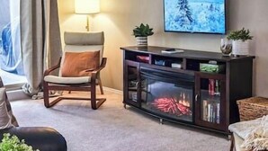 A living room with a modern chair, a glass cabinet with books, a flat-screen TV, and a lamp.