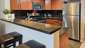 A modern kitchen with wooden cabinets, stainless steel appliances, a granite countertop, and two bar stools.