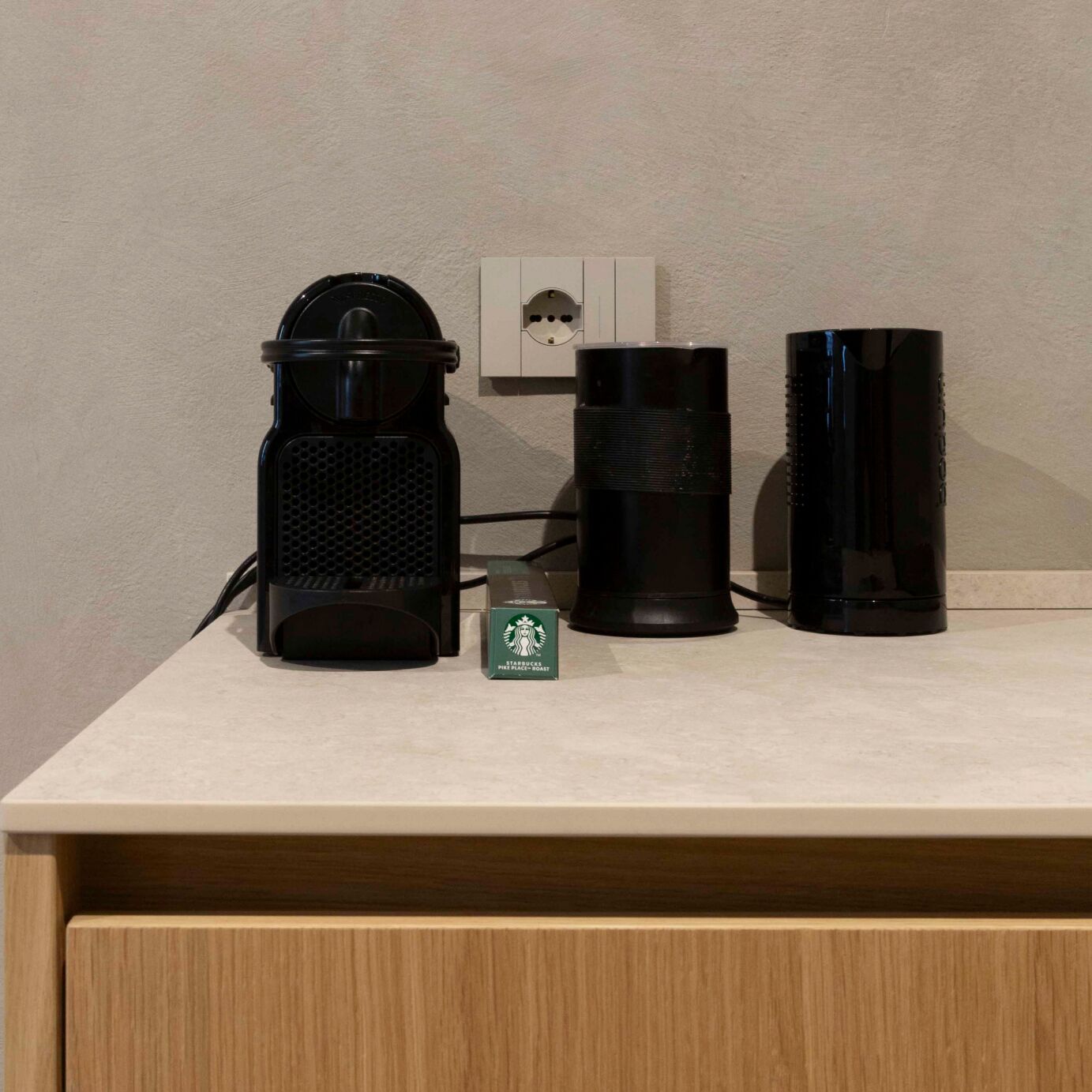 Uma cafeteira, um objeto cilíndrico preto e uma caixa verde da Starbucks em uma bancada.