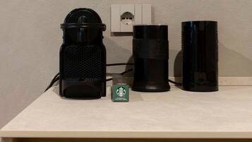 Uma cafeteira, um objeto cilíndrico preto e uma caixa verde da Starbucks em uma bancada.