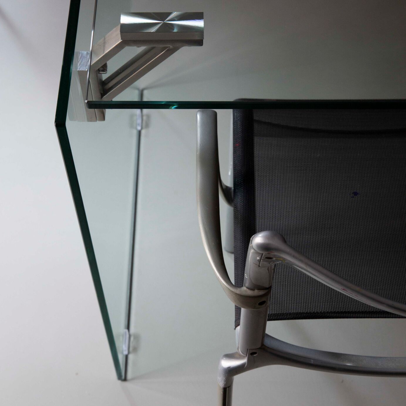 A glass table with a metal frame and a mesh backrest.