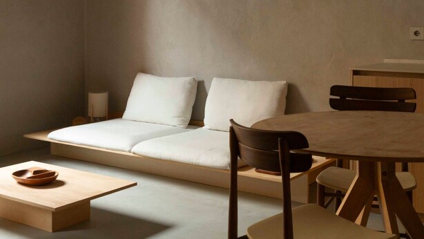 Una habitación moderna y minimalista con un sofá, una mesa de comedor de madera y una mesita auxiliar.
