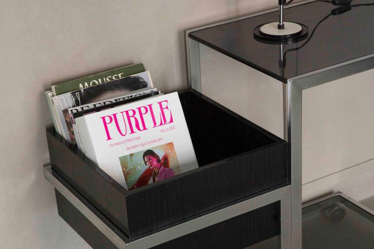 Eine schwarze Aufbewahrungsbox mit Zeitschriften darauf, auf einem schwarzen Tisch neben einem weißen Schrank platziert.