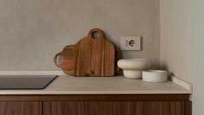 Una encimera de cocina con una tabla de cortar de madera, un enchufe eléctrico blanco y dos cuencos de cerámica blanca.