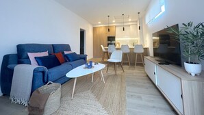 Un soggiorno moderno con un divano blu, un tavolino bianco e un televisore su un mobile in legno.