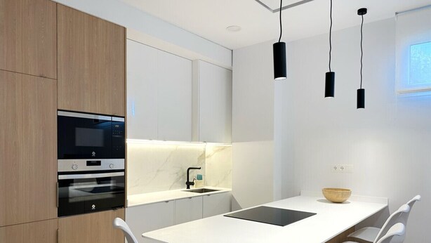 Una cucina moderna con forno integrato, lavello e zona pranzo con tavolo e sedie bianche.