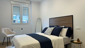 Una camera da letto con un letto, una sedia, uno specchio rotondo e un tavolino con una bottiglia.