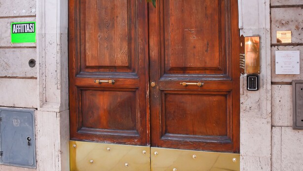Una gran puerta doble de madera con una sección inferior de latón, un cierre con teclado y un letrero verde en la pared a la izquierda.