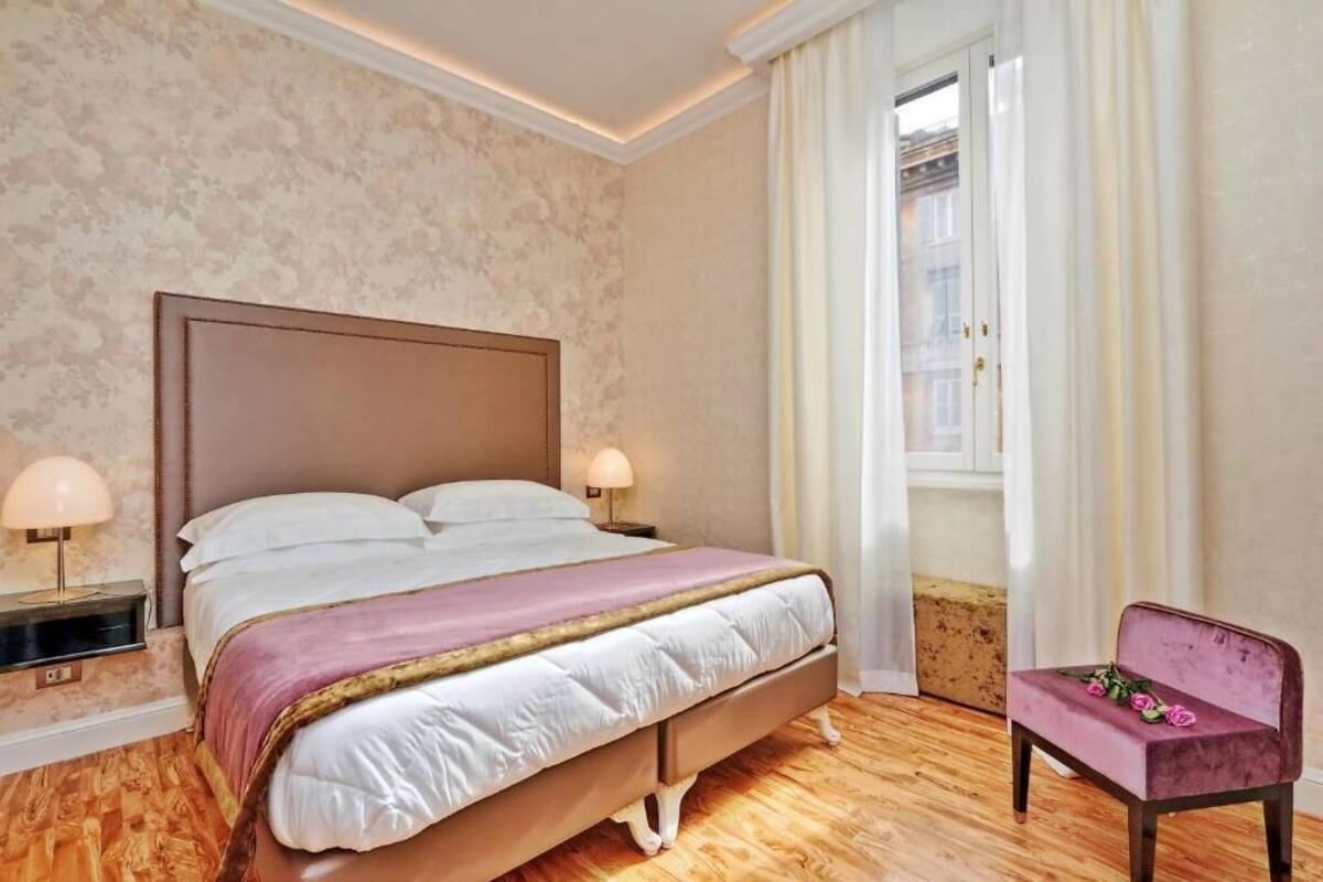 Un dormitorio con una cama grande, lámparas de noche, una ventana con cortinas y una silla.