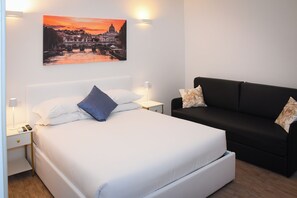Ein ordentlich eingerichtetes Schlafzimmer mit einem Bett, Nachttischen, einem schwarzen Sofa und einem Wandbild.
