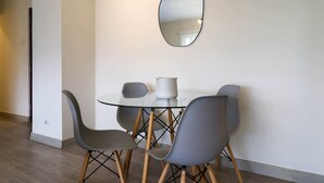 A dining area with a glass table, four grey chairs, a white vase, and a round mirror on the wall. - w*| Fantastic 2BR w/ modern balcony in Miraflores (Lima)