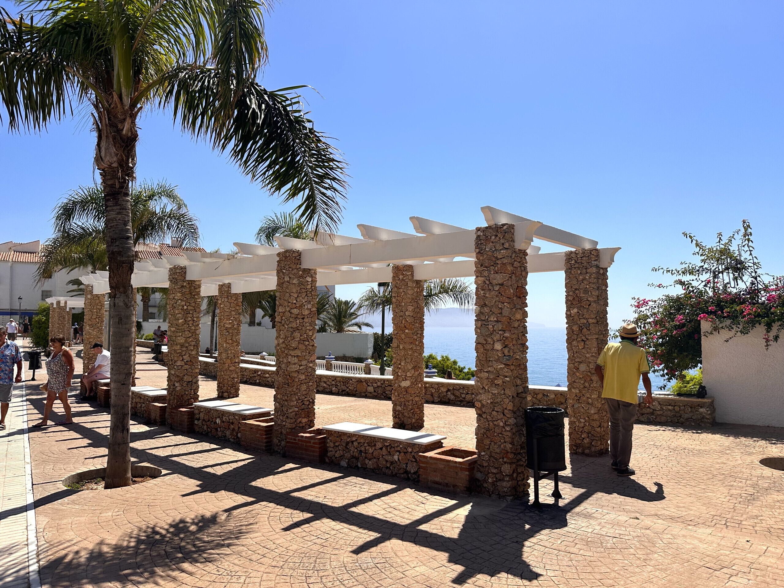 Un espace extérieur aménagé, abrité et doté de piliers en pierre et d’une pergola, offrant une vue sur une étendue d’eau.