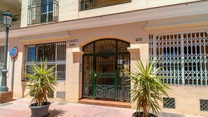 Une entrée d’immeuble avec une porte grillagée, des plantes en pot et un lampadaire.