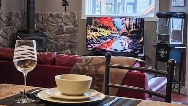 Un salon chaleureux avec un mur en pierre, une cheminée et une grande fenêtre donnant sur la forêt.