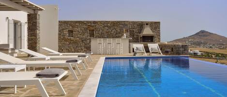 Une piscine à débordement située sur le toit, avec des murs en pierre, des chaises longues et un four en pierre.