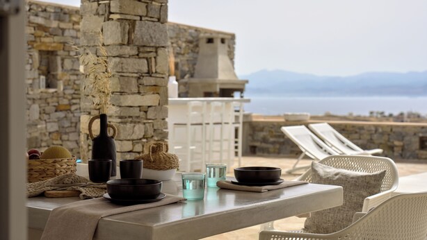 A stone building with a table set for dining, overlooking a body of water.