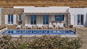 A modern villa with a swimming pool, outdoor seating, and stone walls.