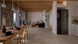 A modern kitchen with a large island, a dining area with a wooden table, and a stone wall.