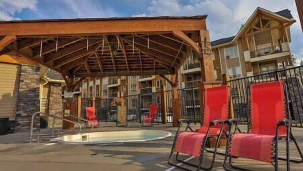 Un espace extérieur avec une piscine, agrémenté d’une pergola en bois, de chaises longues rouges et d’un bâtiment doté de balcons en arrière-plan.