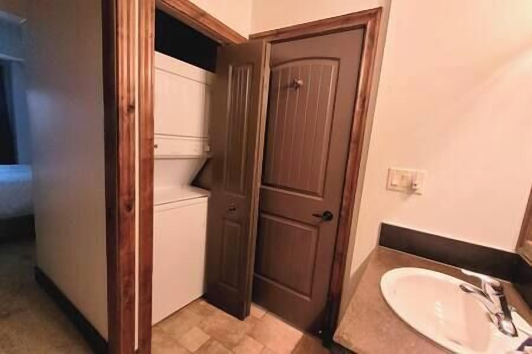 Un baño con un lavabo blanco, una puerta de madera y piso de baldosas.