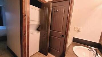 Un baño con un lavabo blanco, una puerta de madera y piso de baldosas.