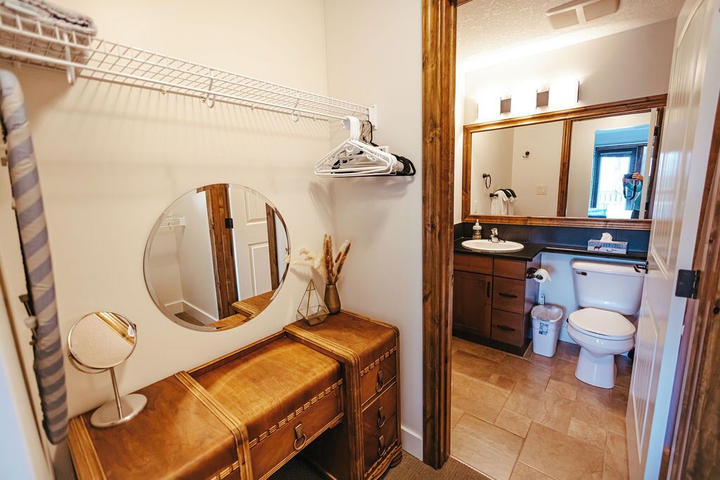 Ein Badezimmer mit einem Holz-Waschtisch, einem runden Spiegel, einem Handtuchhalter und einer Toilette.