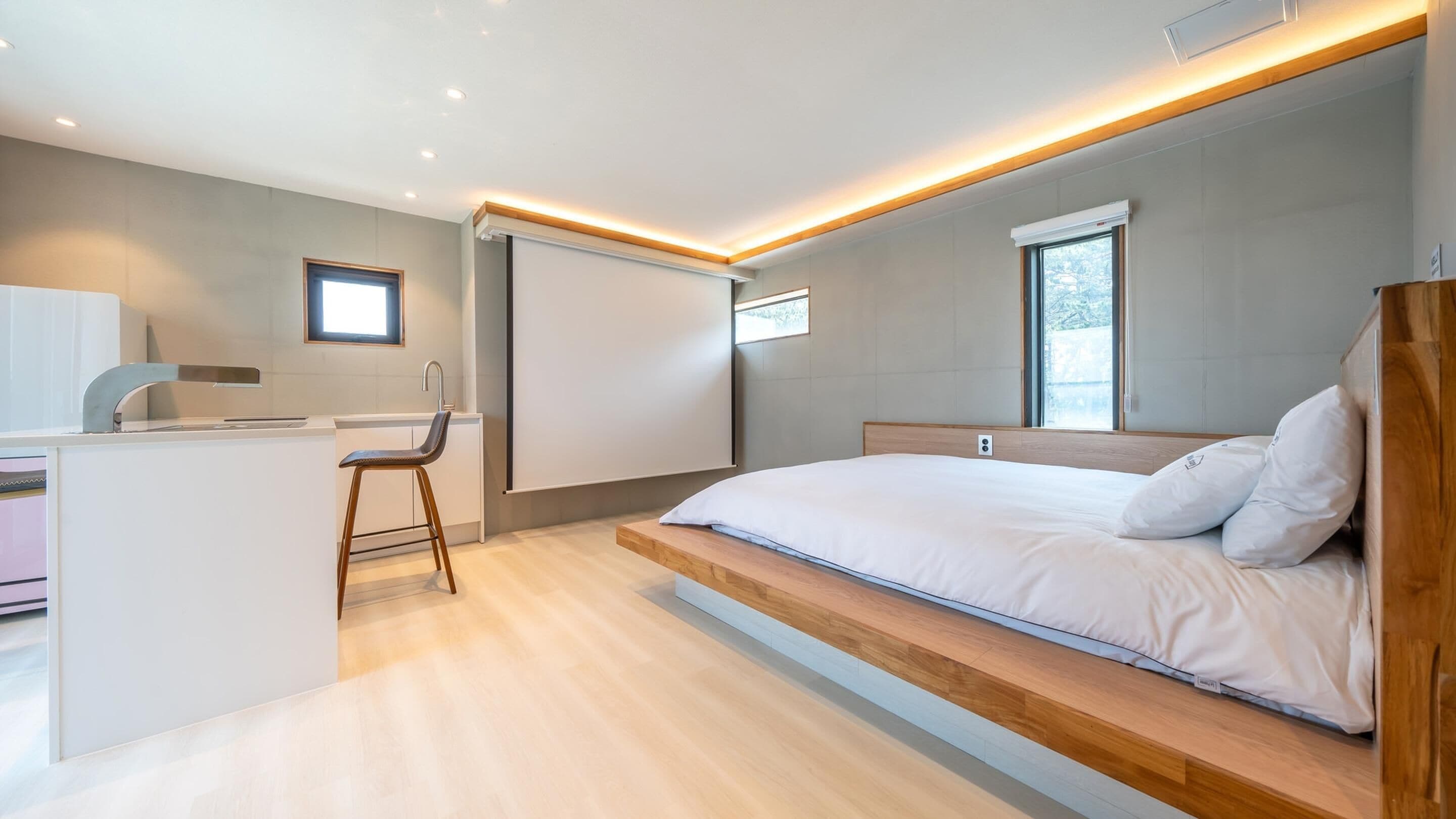 A modern bedroom with a bed, a desk with a chair, and a window.