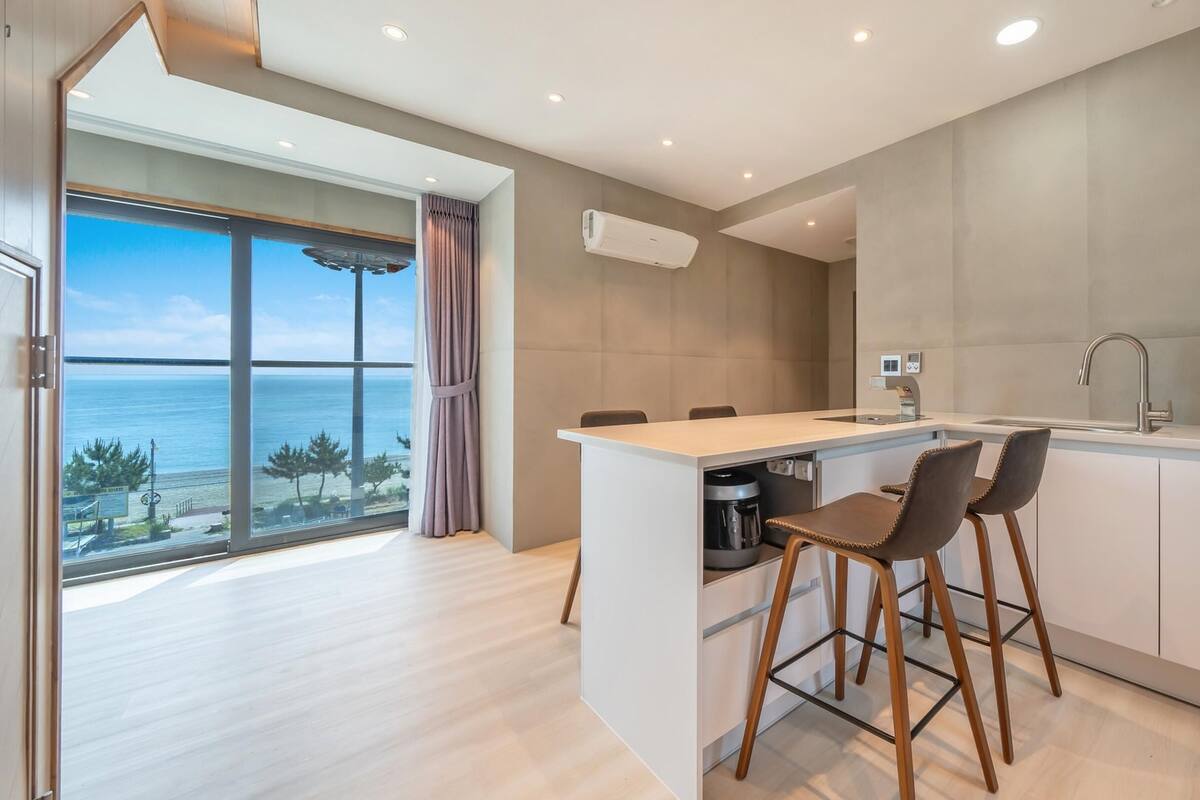 A modern kitchen with a large island, bar stools, and a view of the sea.