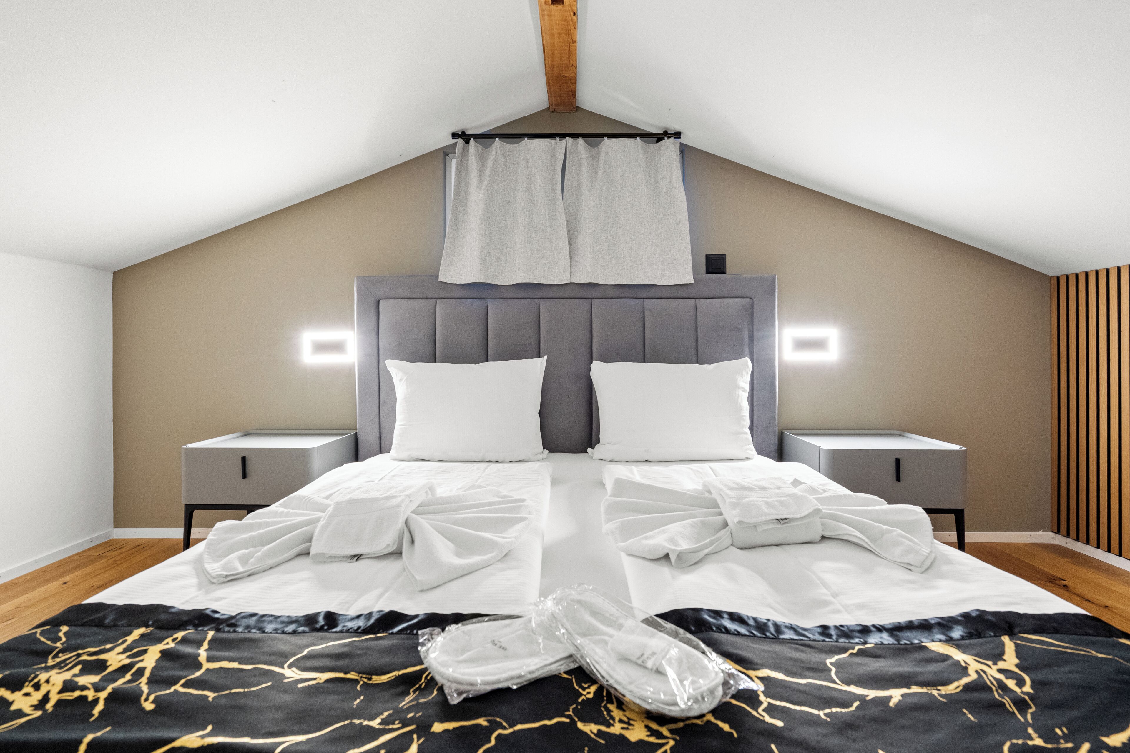 A neatly made bed with white linens, a grey headboard, and a wooden ceiling.