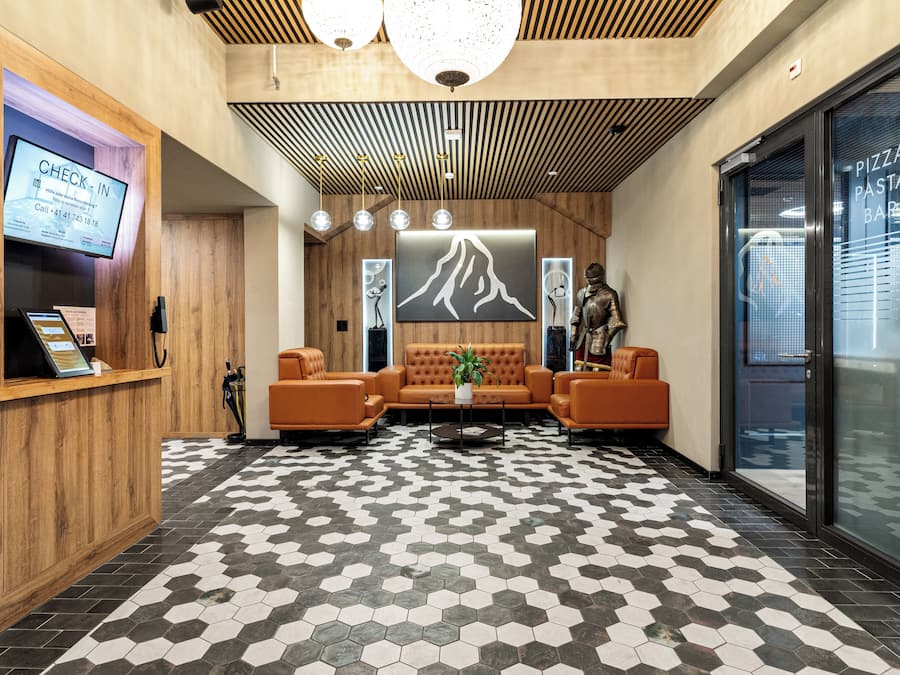 A reception area with a check-in counter, a large screen displaying a check-in message, a sofa, and a patterned floor.