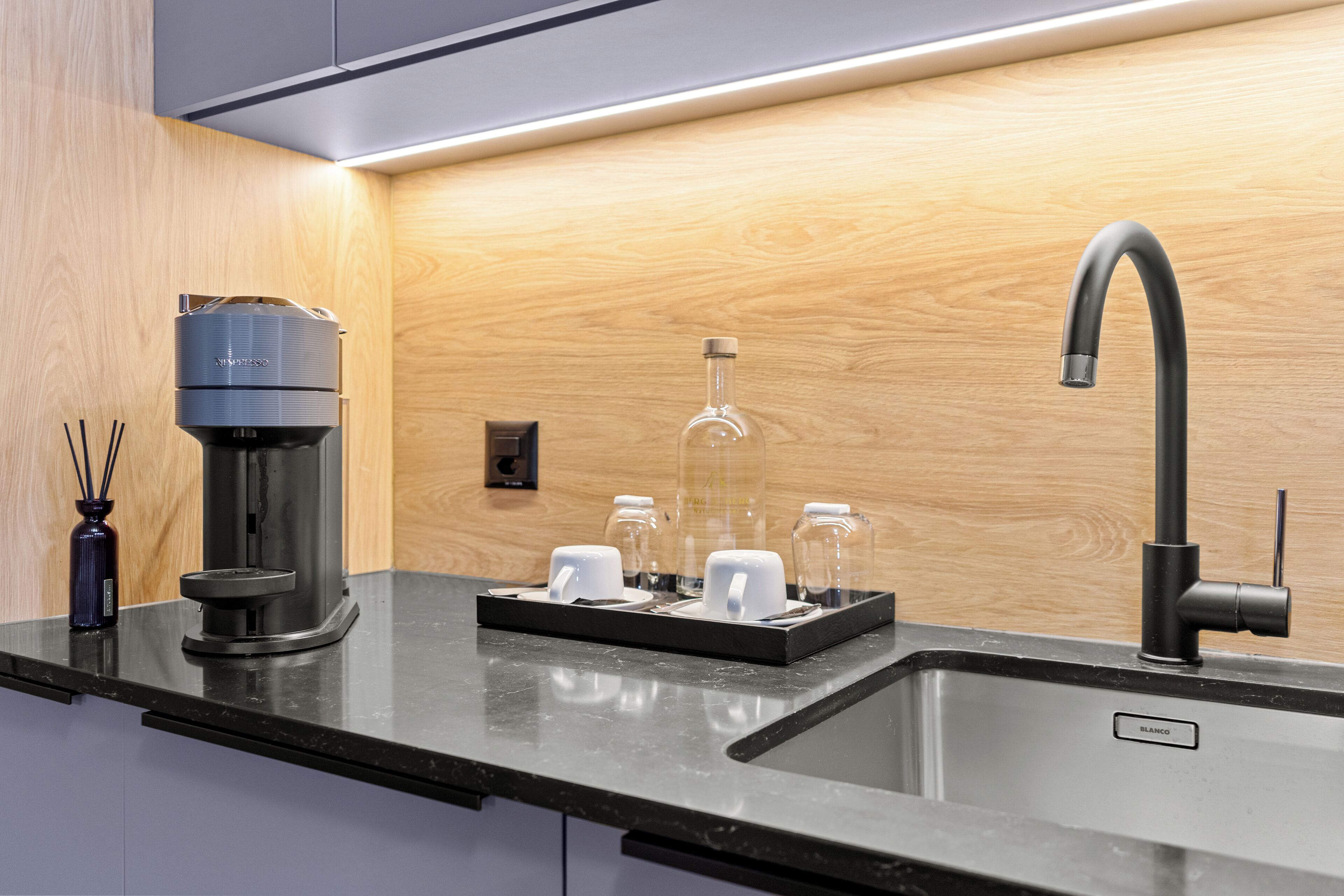 A modern kitchen with a black countertop, a coffee maker, a glass carafe, and a sink.