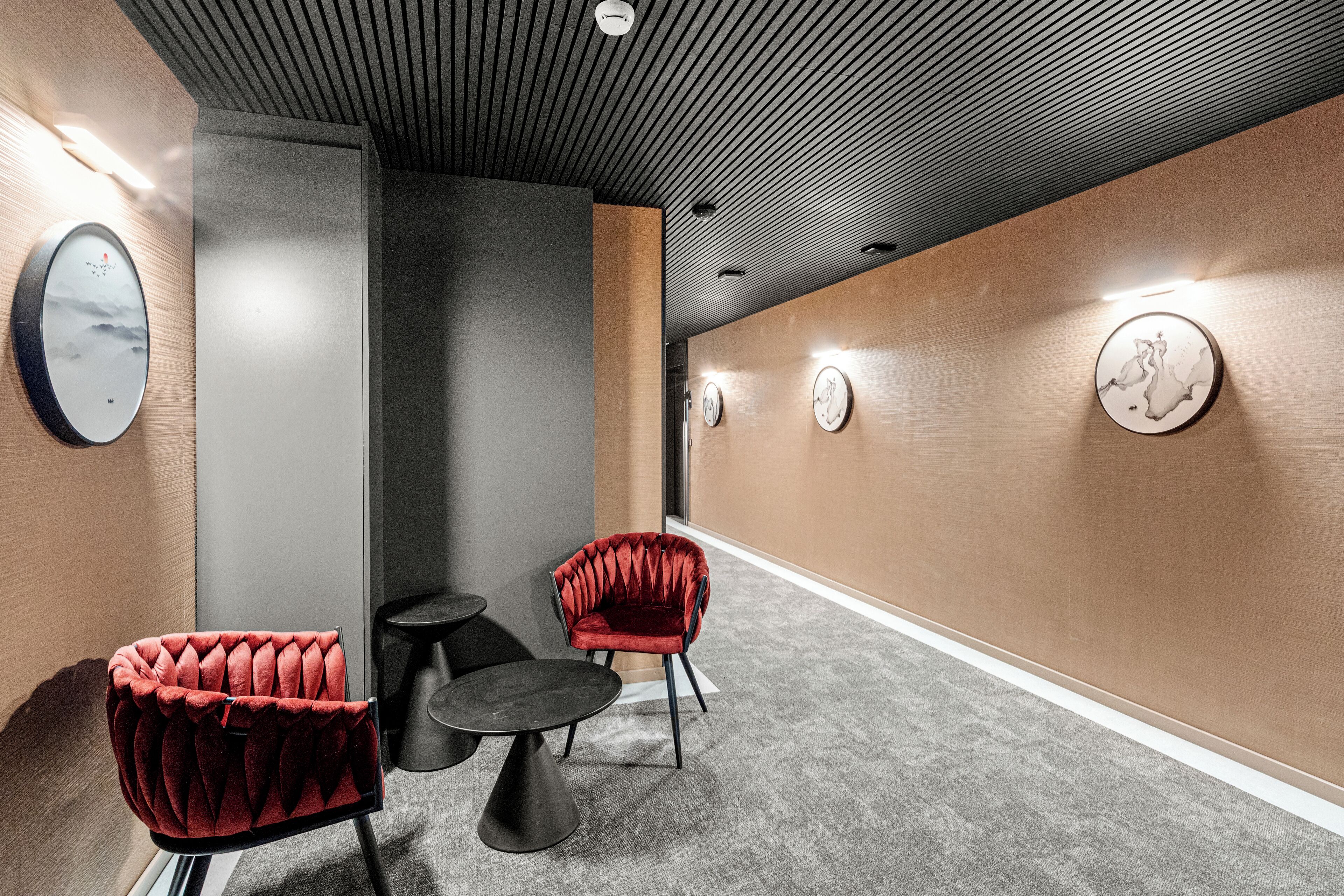 A hallway with a red velvet chair, a small round table, and wall clocks.
