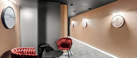 A hallway with a red velvet chair, a small round table, and wall clocks.