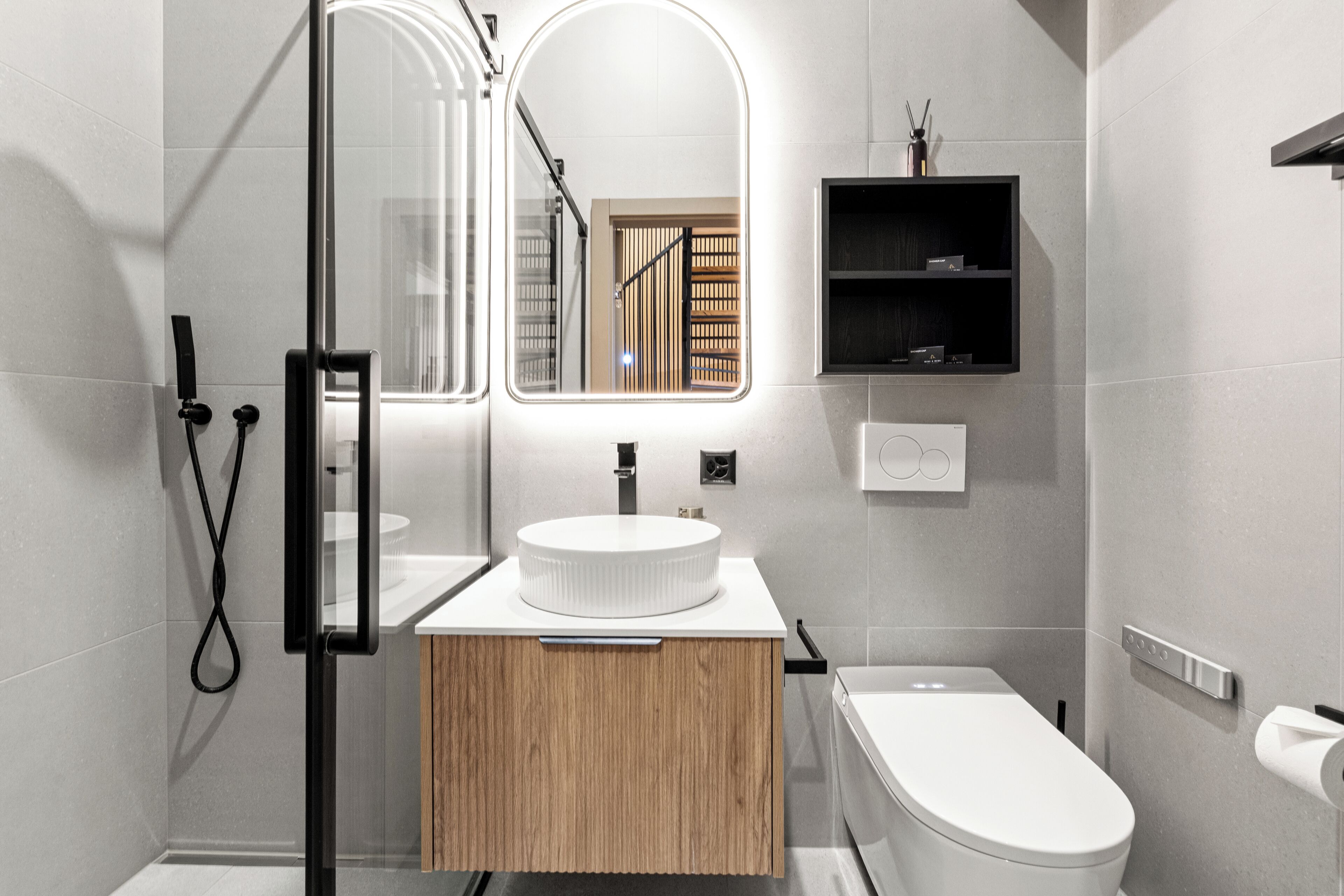 A modern bathroom with a glass shower enclosure, a wooden vanity, a white sink, and a toilet.