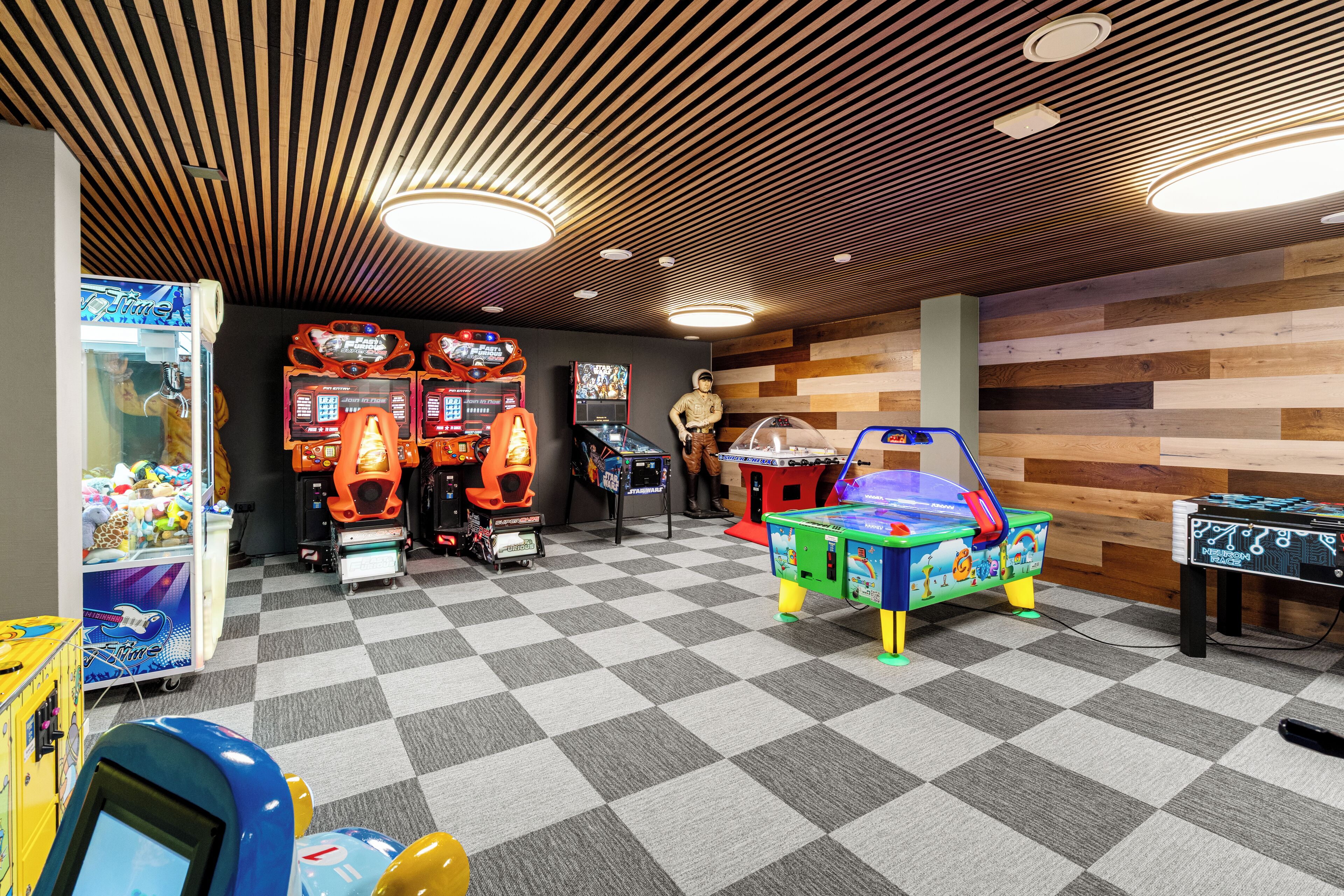 A room with a checkered floor, wooden ceiling, and various arcade games.