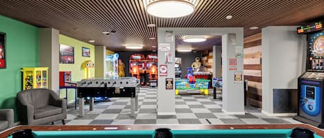A pool table in a room with a checkered floor, a foosball table, and arcade games.