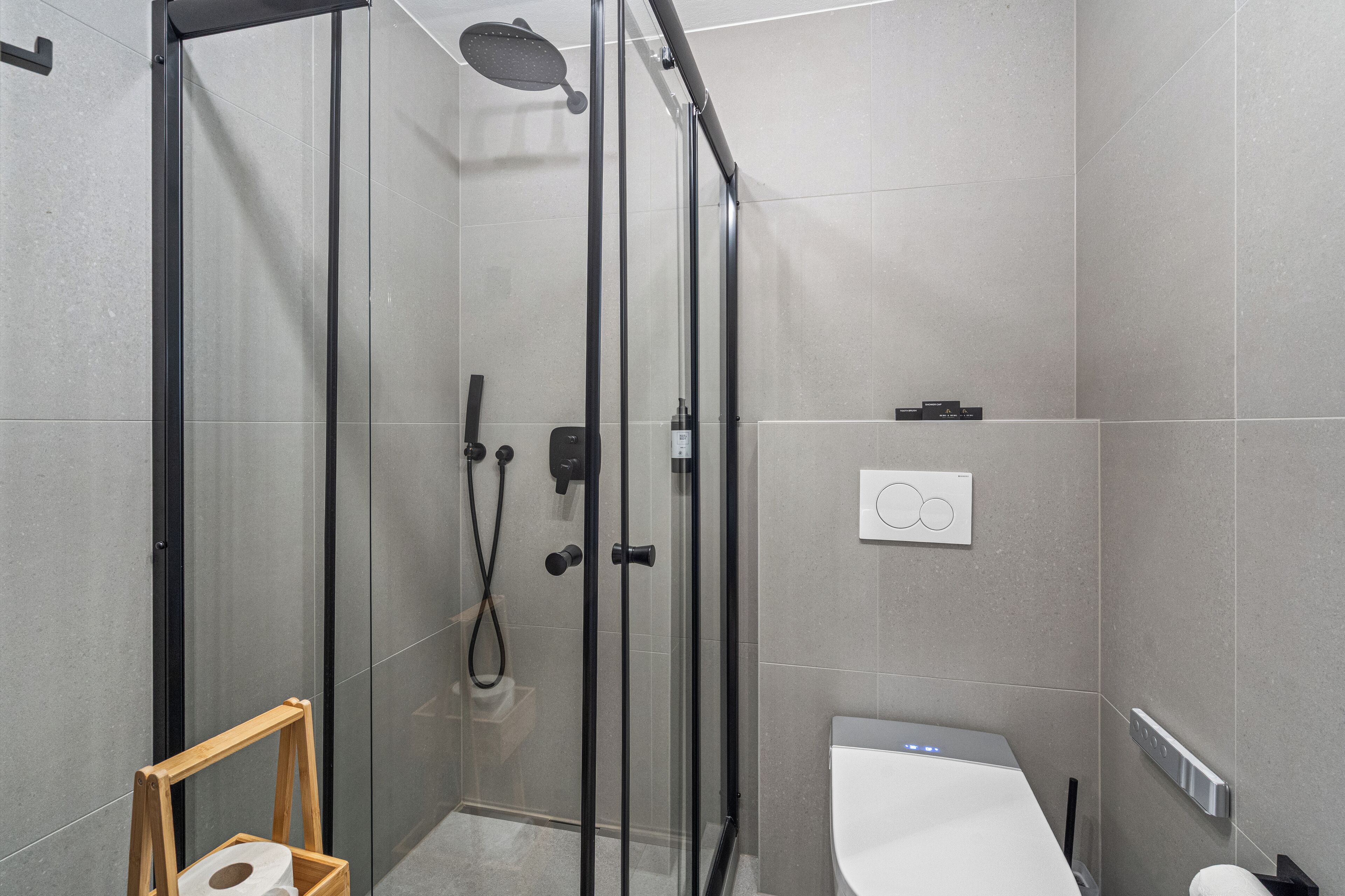A modern bathroom with a glass-enclosed shower, a toilet, and a small wooden stool.