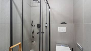 Un baño moderno con ducha de vidrio, inodoro y un pequeño taburete de madera.